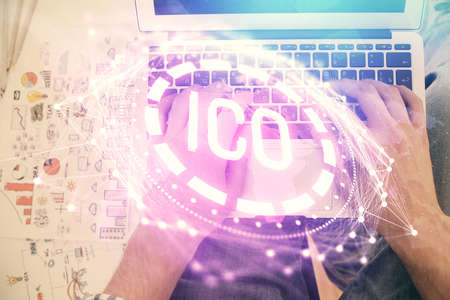Double exposure of man's hands typing over computer keyboard and crypto currency theme hologram...