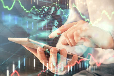 Double exposure of man's hands holding and using a digital device and forex graph drawing. Financial...