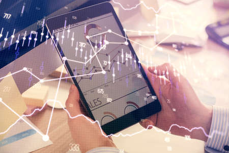 Double exposure of man's hands holding and using a phone and financial graph drawing. Analysis...