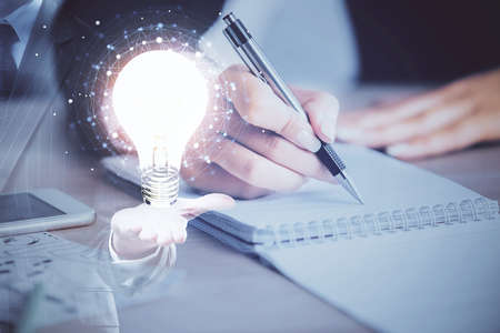 Bulb hologram over hands taking notes background. Concept of idea. Double exposureの写真素材