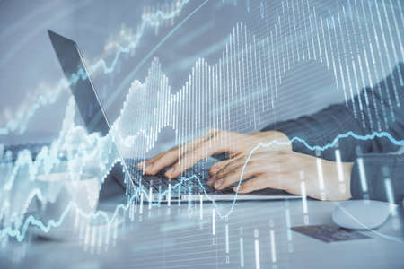 Double exposure of businesswoman hands typing on computer and forex graph hologram drawing....
