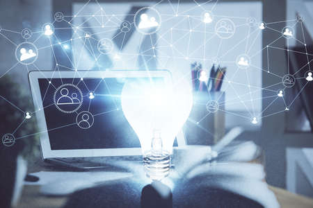Computer on desktop in office with bulb icon hologram. Double exposure. Concept of idea.