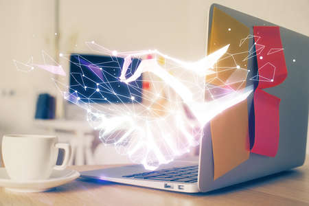 Desktop computer background in office and handshake hologram drawing. Double exposure. Pertnership concept.の写真素材