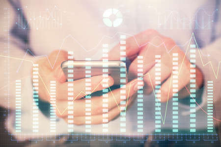 Multi exposure of man's hands holding and using a digital phone and forex graph drawing. Financial...