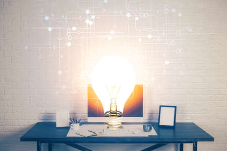 Computer on desktop in office with bulb icon hologram. Double exposure. Concept of idea.