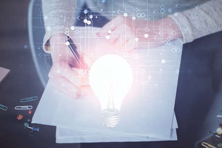 Bulb hologram over hands taking notes background. Concept of idea. Double exposureの写真素材