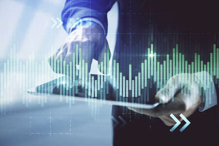 Double exposure of man's hands holding and using a digital device and forex graph drawing. Financial...