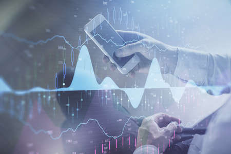 Double exposure of man's hands holding and using a digital device and forex graph drawing. Financial...