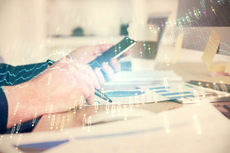 Double exposure of man's hands holding and using a phone and financial graph drawing. Analysis...