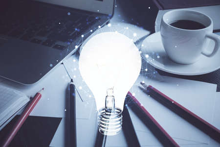 Computer on desktop in office with bulb icon hologram. Double exposure. Concept of idea.