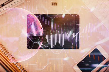 Double exposure of forex graph hologram over desktop with phone. Top view. Mobile trade platform...