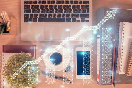 Double exposure of financial graph hologram over desktop with phone. Top view. Mobile trade platform...