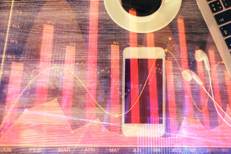 Double exposure of forex chart hologram over desktop with phone. Top view. Mobile trade platform...