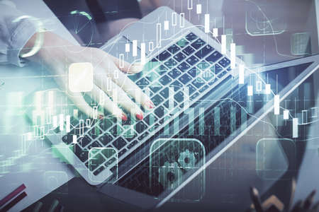 Double exposure of businesswoman hands typing on computer and financial graph hologram drawing....