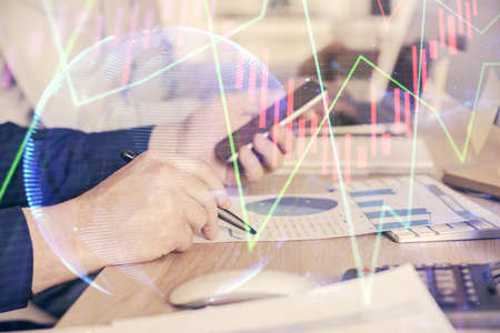 Double exposure of man's hands holding and using a digital device and forex graph drawing. Financial...