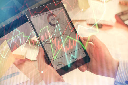 Double exposure of man's hands holding and using a phone and financial graph drawing. Analysis...