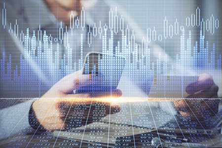 Double exposure of man's hands holding and using a phone and financial graph drawing. Analysis...