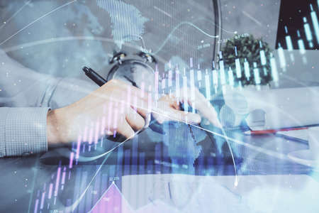 Double exposure of man's hands holding and using a phone and financial graph drawing. Analysis...