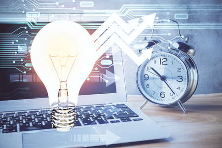 Computer on desktop in office with bulb icon hologram. Double exposure. Concept of idea.