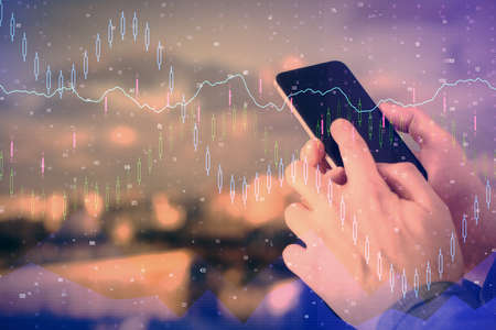 Double exposure of man's hands holding and using a digital device and forex graph drawing. Financial...