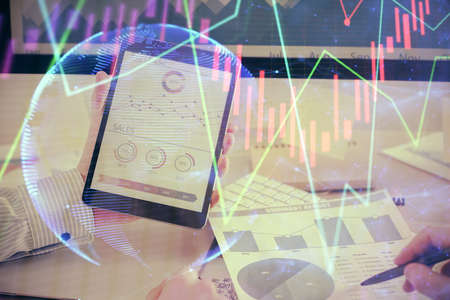 Double exposure of man's hands holding and using a digital device and forex graph drawing. Financial...