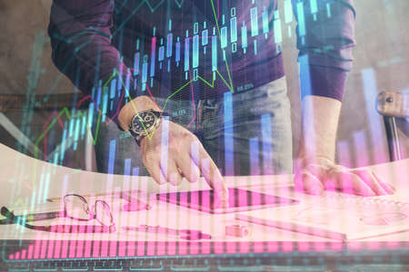 Double exposure of man's hands holding and using a digital device and forex graph drawing. Financial...