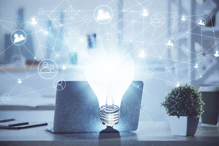 Computer on desktop in office with bulb icon hologram. Double exposure. Concept of idea.の写真素材