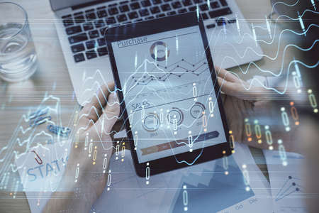 Double exposure of man's hands holding and using a digital device and forex graph drawing. Financial...