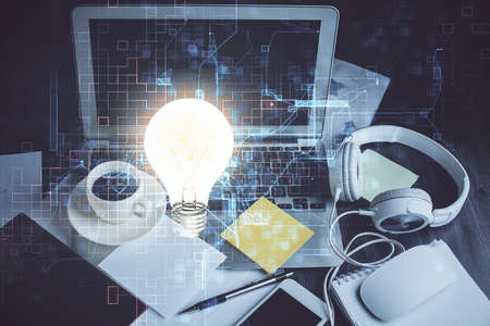 Computer on desktop in office with bulb icon hologram. Double exposure. Concept of idea.の写真素材