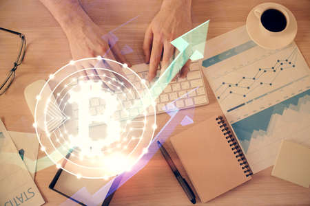 Double exposure of man's hands typing over computer keyboard and crypto currency theme hologram...