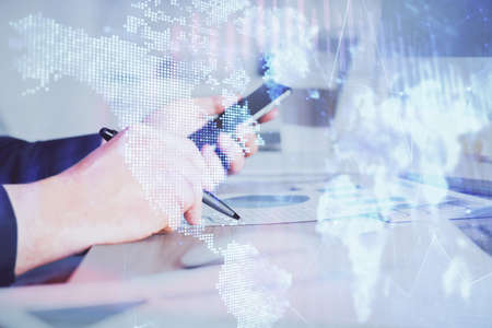 Double exposure of man's hands holding and using a phone and financial graph drawing. Analysis...