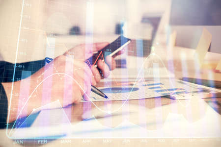 Double exposure of man's hands holding and using a phone and financial graph drawing. Analysis...