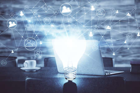 Computer on desktop in office with bulb icon hologram. Double exposure. Concept of idea.