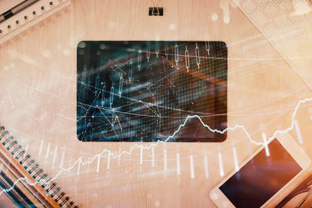 Double exposure of forex graph hologram over desktop with phone. Top view. Mobile trade platform...