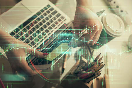 Double exposure of businesswoman hands typing on computer and financial graph hologram drawing....