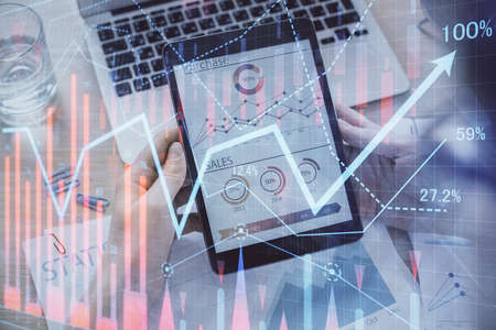 Double exposure of man's hands holding and using a digital device and forex graph drawing. Financial...