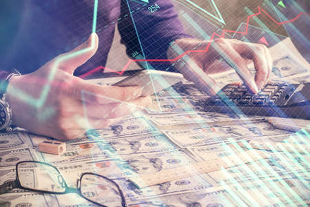 Double exposure of man's hands holding and using a digital device and forex graph drawing. Financial...