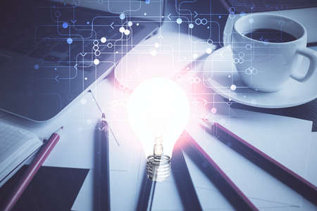 Computer on desktop in office with bulb icon hologram. Double exposure. Concept of idea.
