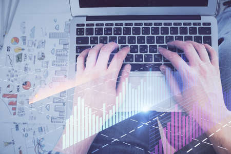 Double exposure of man's hands typing over laptop keyboard and forex chart hologram drawing. Top...