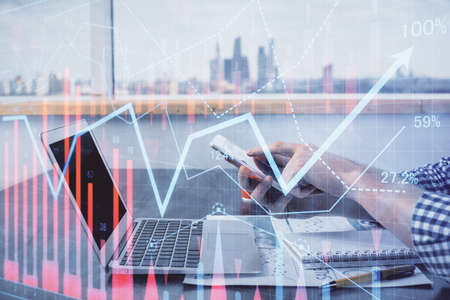 Double exposure of man's hands holding and using a digital device and forex graph drawing. Financial...