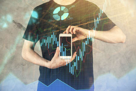 Double exposure of man's hands holding and using a digital device and forex graph drawing. Financial...