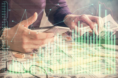 Double exposure of man's hands holding and using a digital device and forex graph drawing. Financial market concept.の写真素材