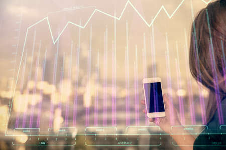 Double exposure of forex chart sketch hologram and woman holding and using a mobile device. Stock market concept.の写真素材