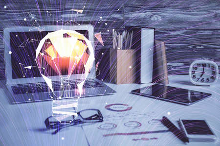 Computer on desktop in office with bulb icon hologram. Double exposure. Concept of idea.の写真素材