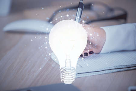 Bulb hologram over hands taking notes background. Concept of idea. Double exposureの写真素材