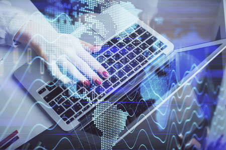 Double exposure of businesswoman hands typing on computer and financial graph hologram drawing....