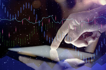 Double exposure of man's hands holding and using a digital device and forex graph drawing. Financial...