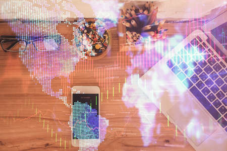 Double exposure of financial graph hologram over desktop with phone. Top view. Mobile trade platform...