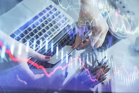 Double exposure of businesswoman hands typing on computer and financial graph hologram drawing....