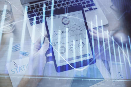 Double exposure of man's hands holding and using a digital device and forex graph drawing. Financial...